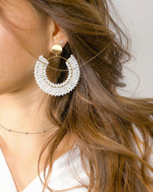 Close-up of a woman wearing a gold and white beaded hoop earring.
