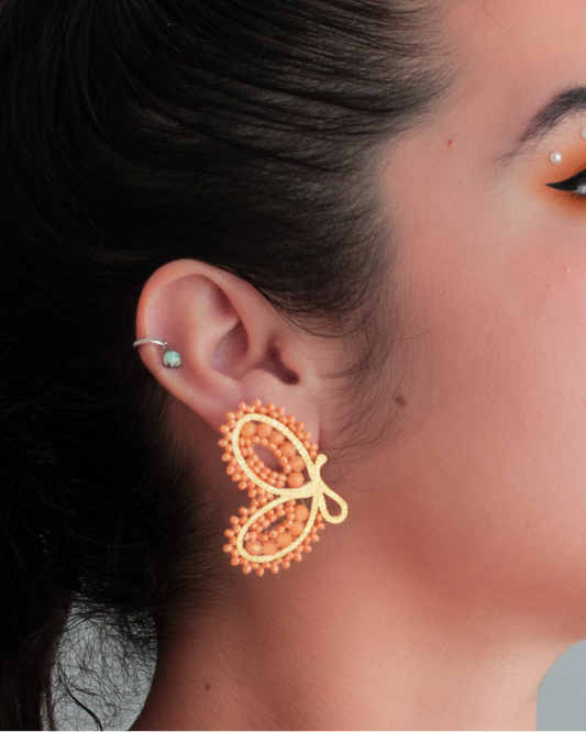 Close-up of a woman wearing a gold butterfly earring against a neutral background