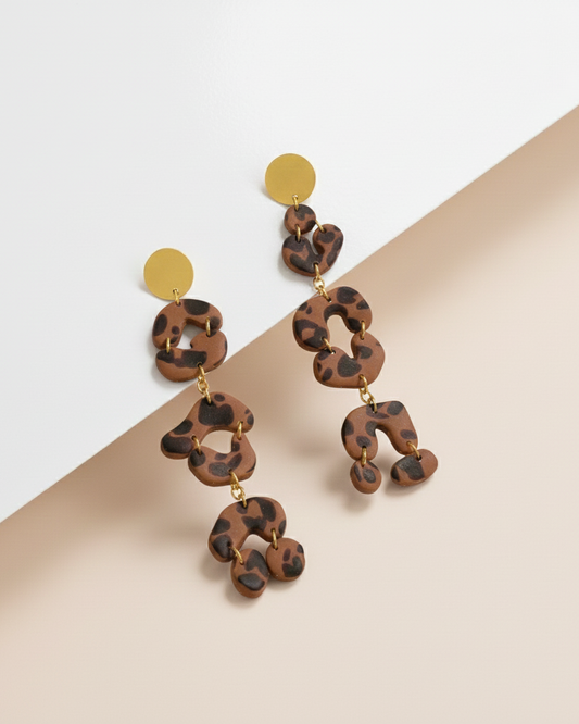 Leopard print Kawami earrings with gold accents on a beige and white background