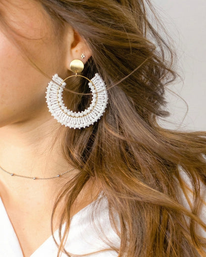 Close-up of a woman wearing a gold and white beaded hoop earring.