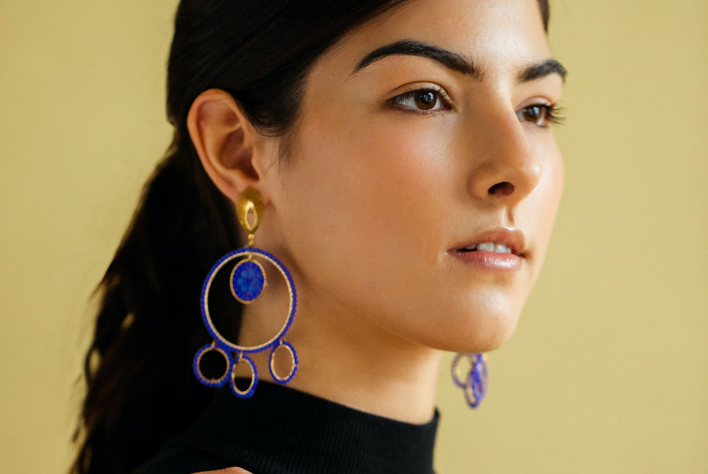 Woman wearing large kawami blue hoop earrings against a beige background