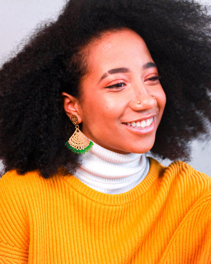 Woman with an afro wearing a yellow sweater, and green and gold kawami earrings against a gray background