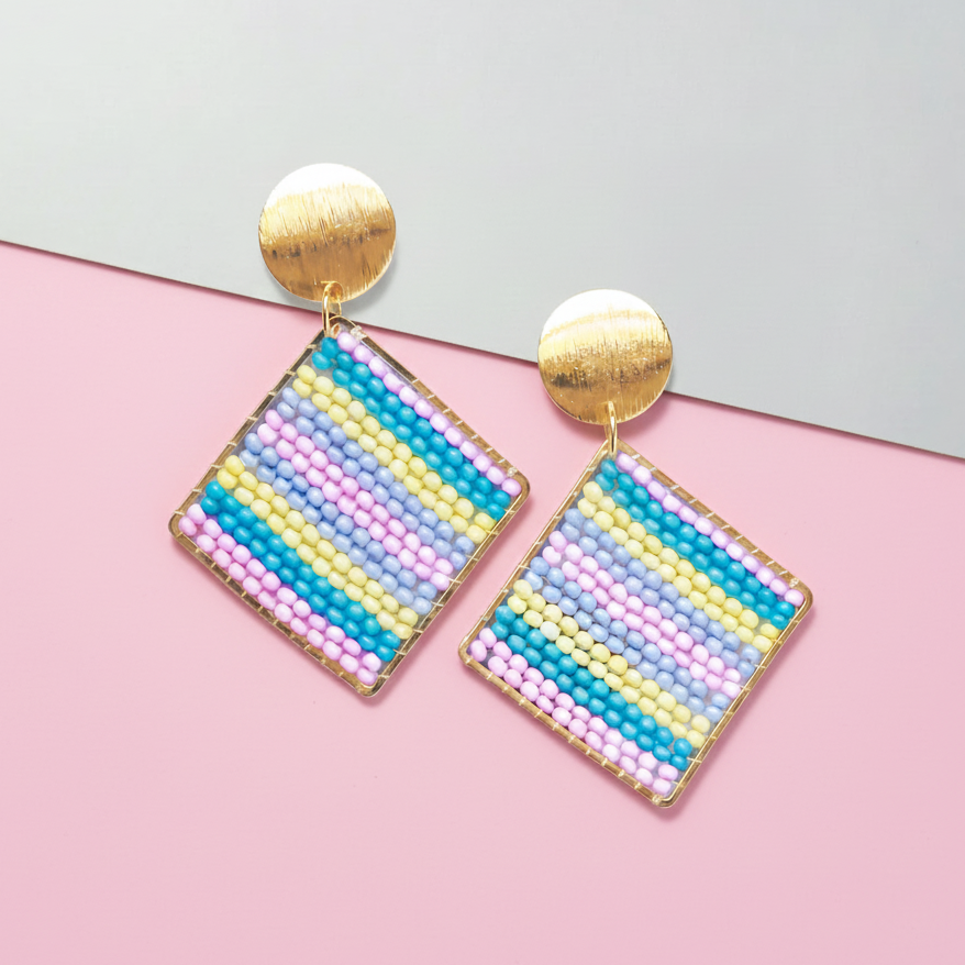 Colorful beaded square Kawami earrings with gold posts on a pink and gray background