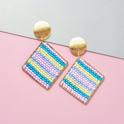 Colorful beaded square Kawami earrings with gold posts on a pink and gray background