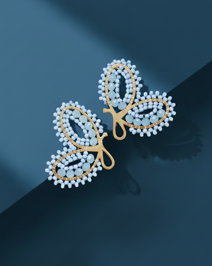 Pair of gold and pearl butterfly-shaped Kawami earrings on a dark blue background