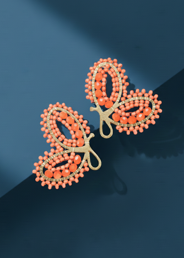 Butterfly-shaped Kawami earrings with orange/coral beads on a dark blue background