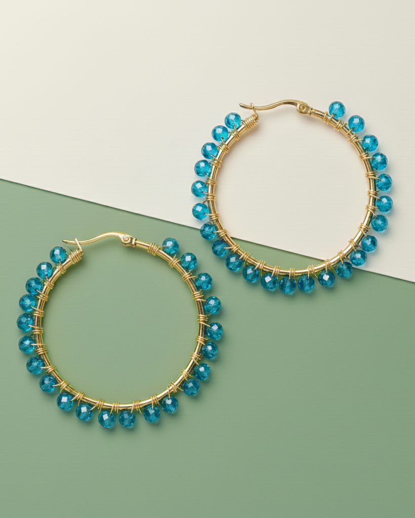 Gold hoop Kawami earrings with blue beads on a green and beige background