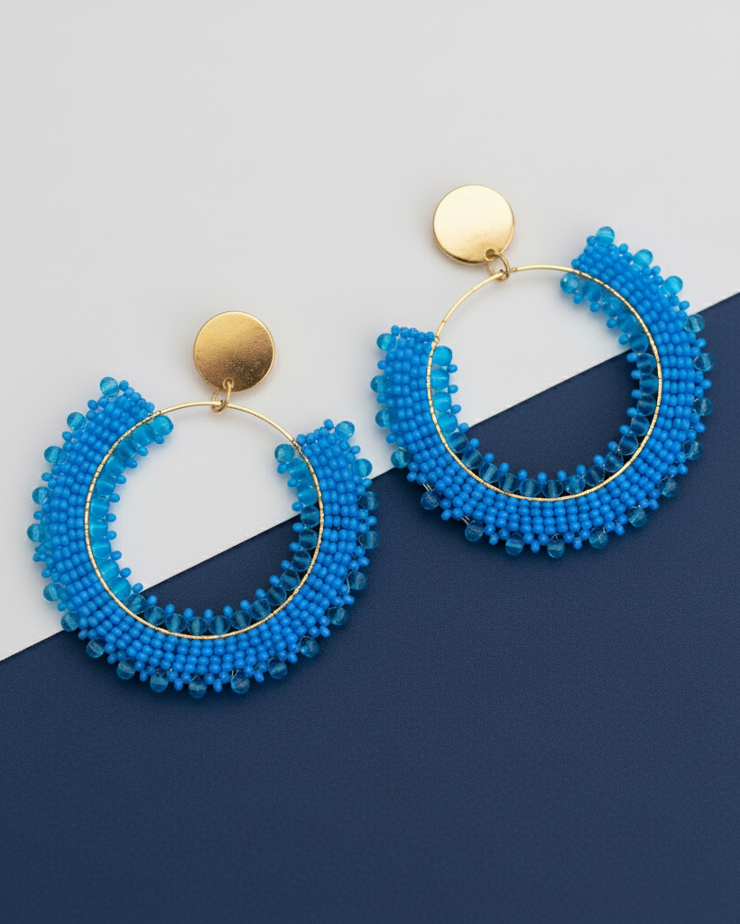 Blue beaded hoop Kawami earrings with gold accents on a two-tone blue background