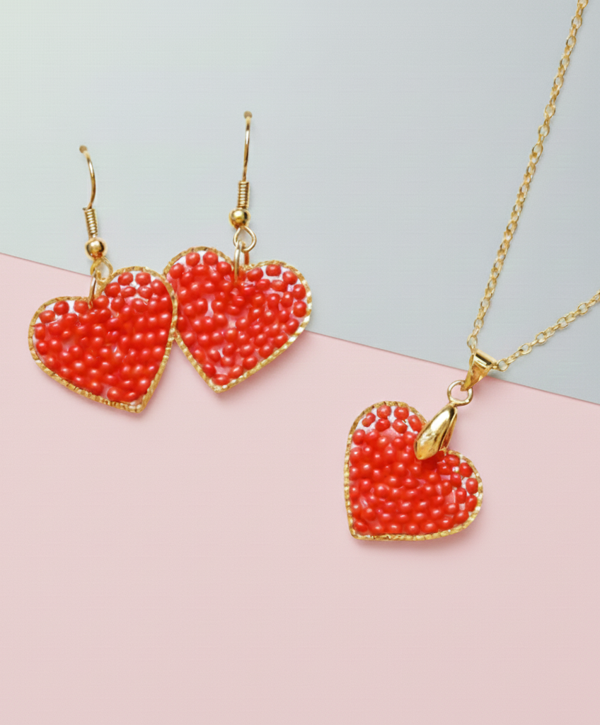 Heart-shaped Kawami jewelry earrings and necklace set with red beads and gold accents on a pink and gray background