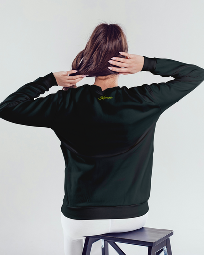 Person wearing a dark jacket with a logo on the back, sitting on a stool against a white background.