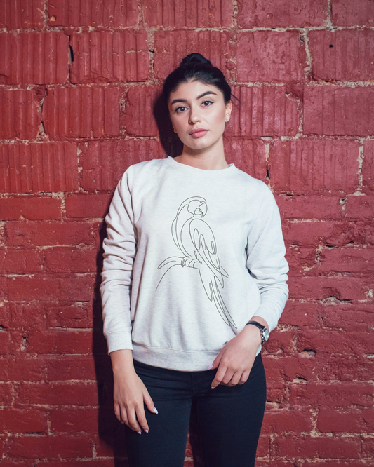 Person wearing a white sweatshirt with a parrot design against a red brick wall