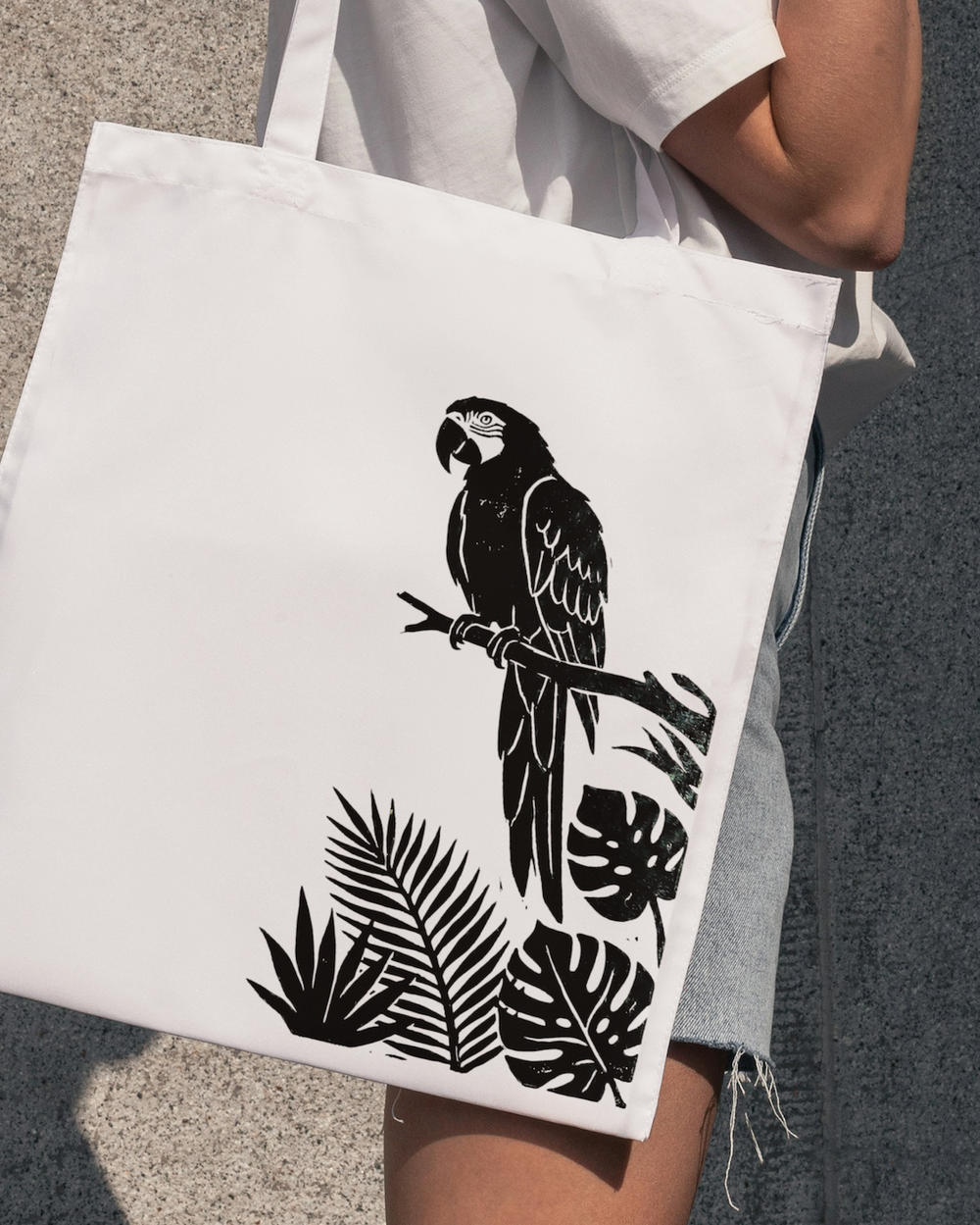 Person holding a tote bag with a black parrot and leaf design on a gray background