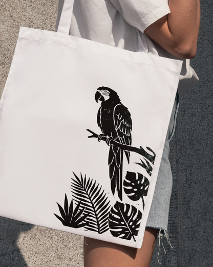 Person holding a tote bag with a black parrot and leaf design on a gray background