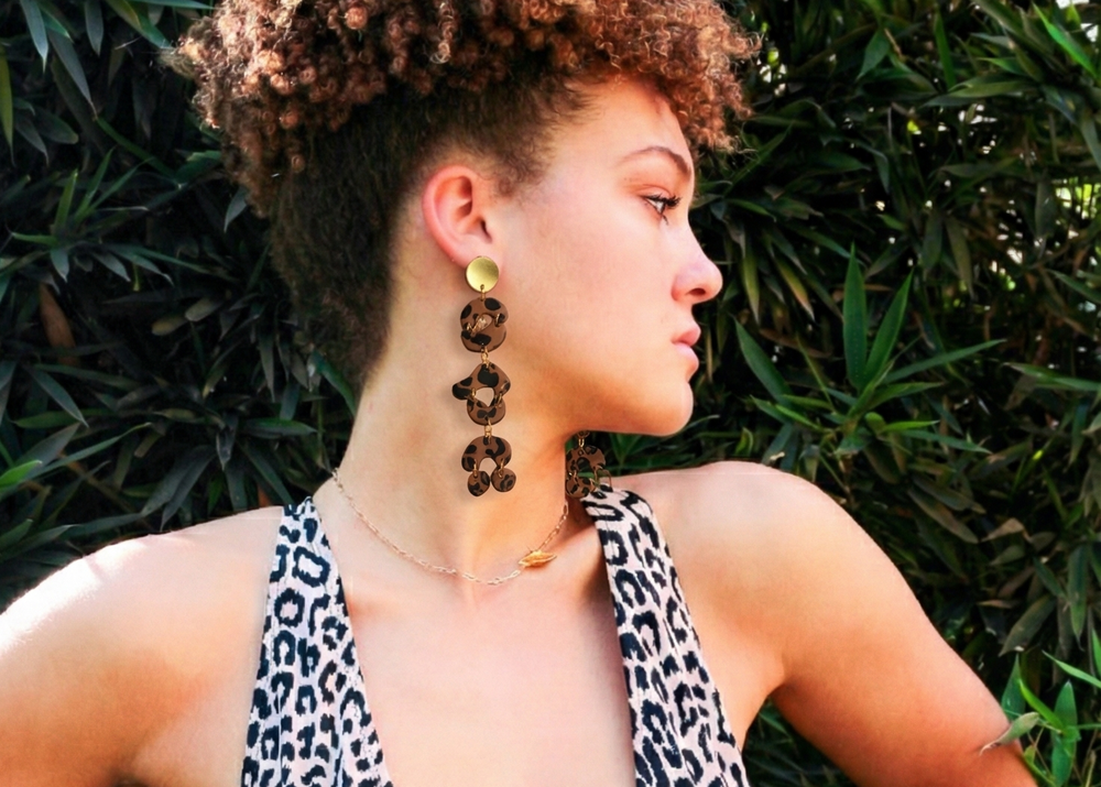 Woman wearing Kawami leopard print earrings and top against a green leafy background