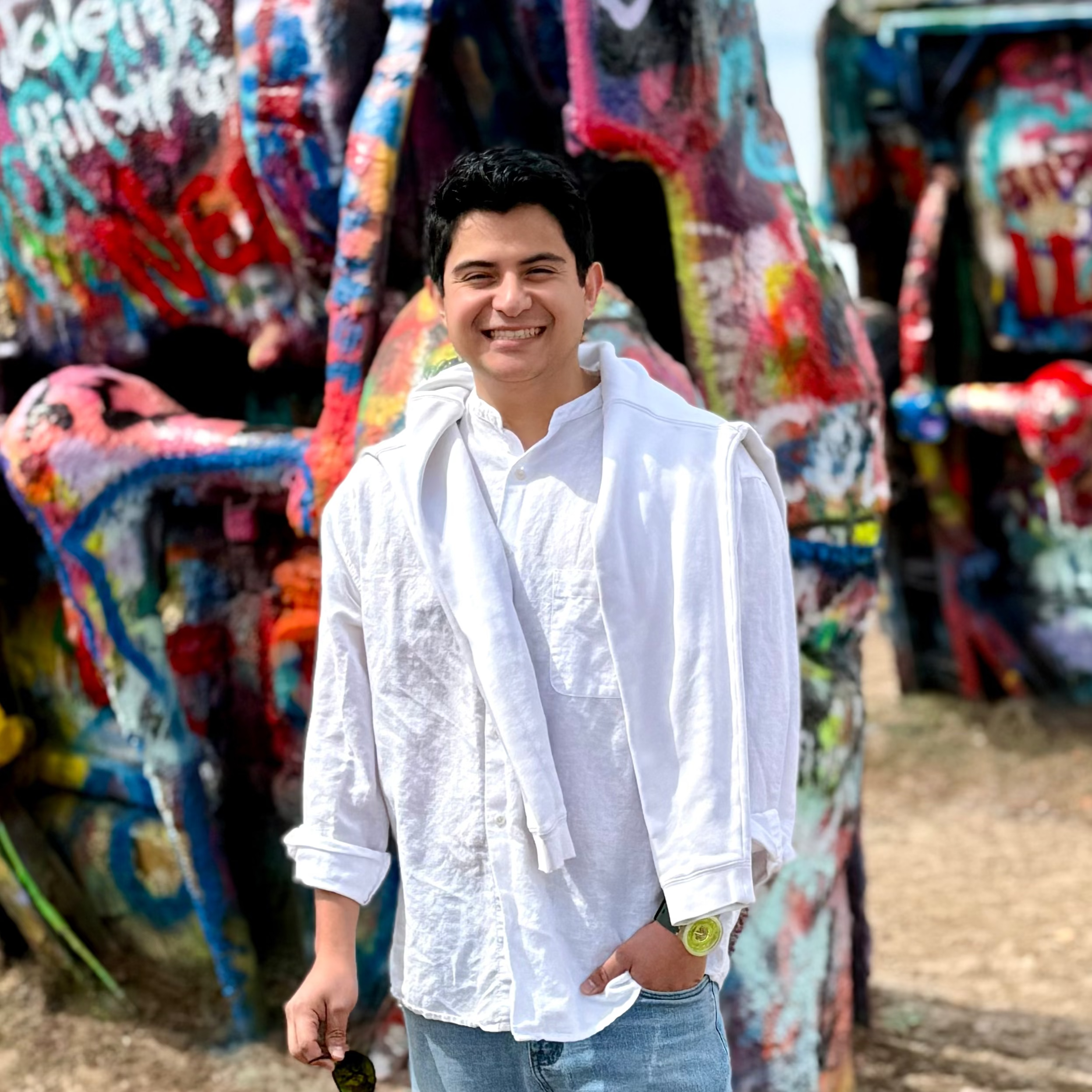 Man standing in front of a colorful art installation with 'Cadillac Ranch' in the background.
