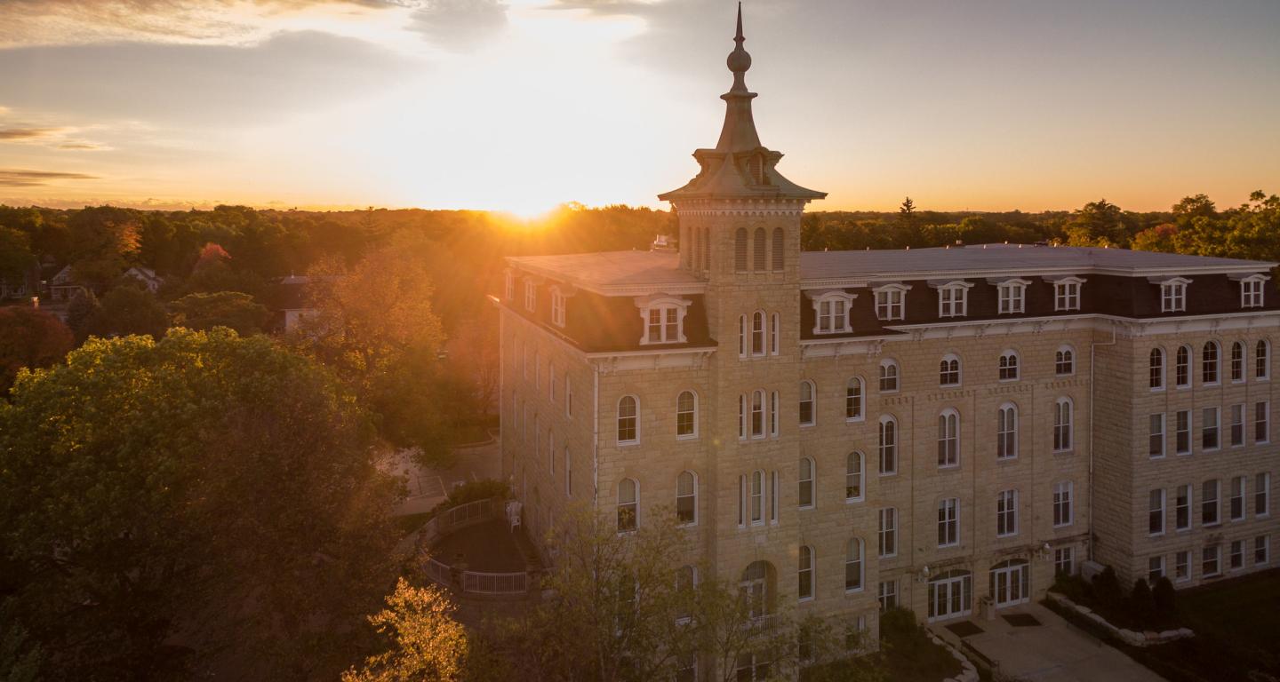 Large building with a clock tower at sunset, surrounded by trees.
