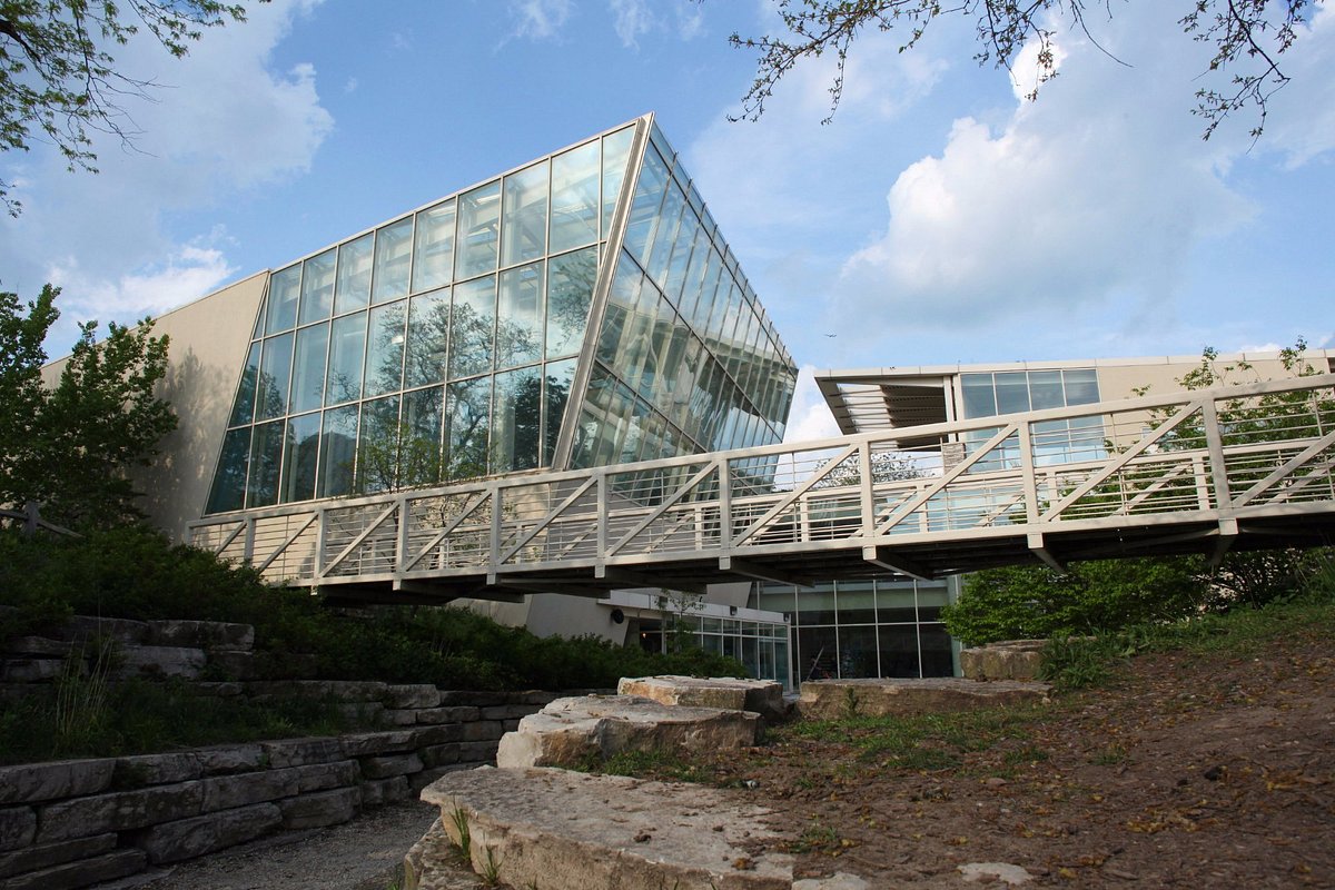 Modern building with glass facade and wooden walkway, surrounded by greenery