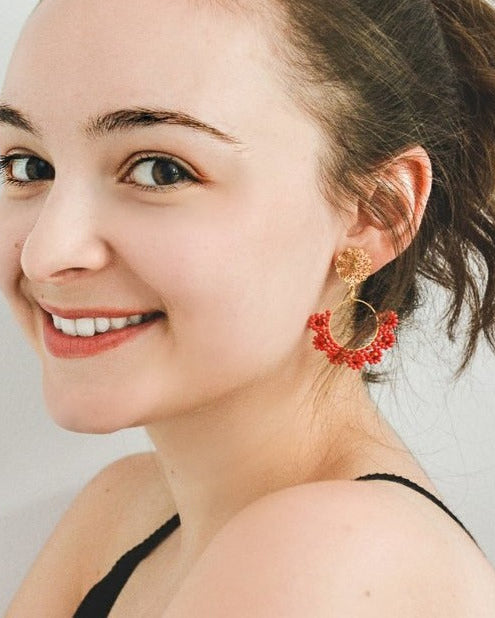 Woman wearing red floral hoop earrings with a neutral background